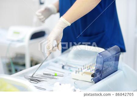 Surgeon or assistant takes sterile instrument during operation in clinic. Steel medical instruments are ready to be used. Modern equipment, tools and technology for surgery. 86842705
