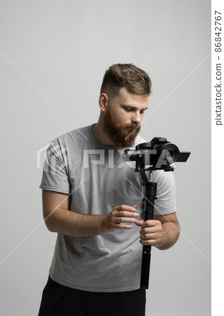 Professional bearded videographer filmmaker cinematographer dop holding camera which set on 3-axis gimbal. Pro equipment helps to make high quality video without shaking. 86842767