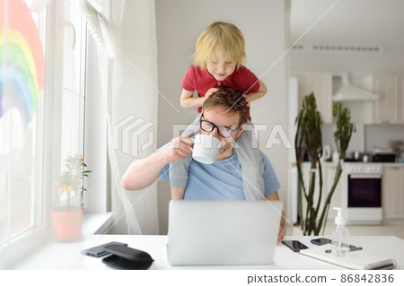 Man is working from home with laptop during quarantine. Home office and parenthood at same time. Exhausted parent with hyperactive child. Man is working from home with laptop during quarantine. Home office and parenthood at same time. Exhausted parent with hyperactive child. 86842836
