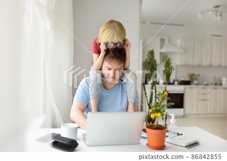 Man is working from home with laptop during quarantine. Home office and parenthood at same time. Exhausted parent with hyperactive child. Man is working from home with laptop during quarantine. Home office and parenthood at same time. Exhausted parent with hyperactive child. 86842855