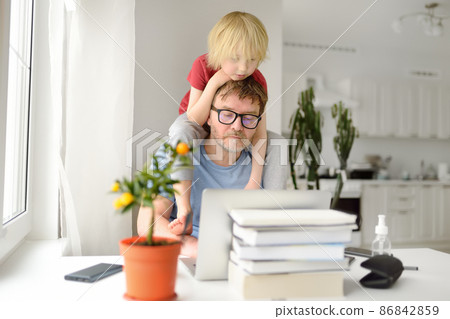 Man is working from home with laptop during quarantine. Home office and parenthood at same time. Exhausted parent with hyperactive child. Man is working from home with laptop during quarantine. Home office and parenthood at same time. Exhausted parent with hyperactive child. 86842859