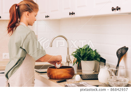 Cute teenage girl in kitchen apron prepares and kneads products for making dough for baking 86842937