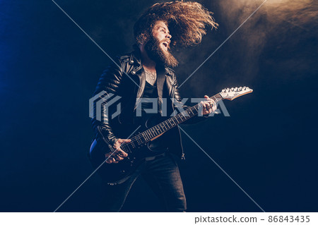 Emotional man rock guitar player with long hair and beard plays on the smoke background. Studio shot Emotional man rock guitar player with long hair and beard plays on the smoke background. Studio shot 86843435