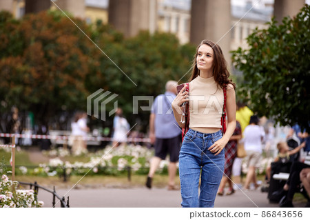 Slender woman stands on city street in jeans at daytime. 86843656