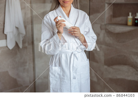 Smiling woman holding cosmetic vial in shower 86844103