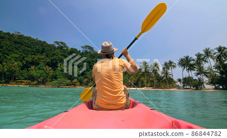 Man with sunglasses and hat rows pink plastic canoe along sea ag 86844782