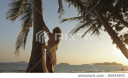 Woman drinking pineapple cocktail Pina Colada near palm tree, in white shirt, sunglasses. Concept rest tropical sea traveling tourism summer holidays Woman drinking pineapple cocktail Pina Colada near palm tree, in white shirt, sunglasses. Concept rest tropical sea traveling tourism summer holidays 86844845
