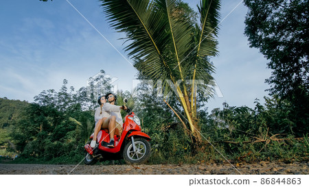 Scooter road trip. Love couple on red motorbike in white clothes on forest road trail. Just married woman and man kiss, hugs, sit on motorbike. Scooter road trip. Love couple on red motorbike in white clothes on forest road trail. Just married woman and man kiss, hugs, sit on motorbike. 86844863