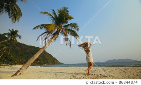 Woman in a White Tunic on Beach, near the Sea, Palm Tree. Blonde 86844874