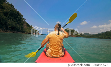 Man with sunglasses and hat rows pink plastic canoe along sea ag 86844878