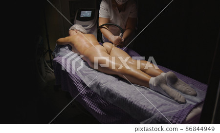 Woman receiving anti-ageing anti-cellulite massage vacuum rf lifting in spa salon. Wellness body and skin care. Black dark background Woman receiving anti-ageing anti-cellulite massage vacuum rf lifting in spa salon. Wellness body and skin care. Black dark background 86844949