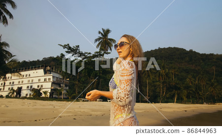Woman in a white tunic on the beach, near the stormy sea. Blonde 86844963