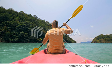 Man with sunglasses and hat rows pink plastic canoe along sea ag 86847343