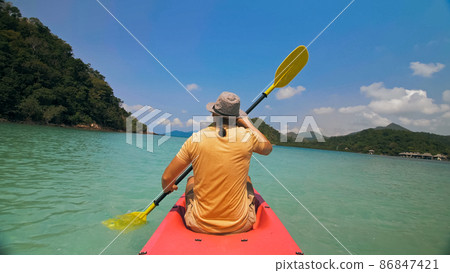Man with sunglasses and hat rows pink plastic canoe along sea ag 86847421