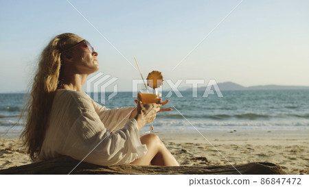 Woman sitting in white dress drinks pineapple cocktail Pina Cola 86847472