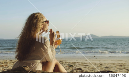 Woman sitting in white dress drinks pineapple cocktail Pina Cola Woman sitting in white dress drinks pineapple cocktail Pina Cola 86847498