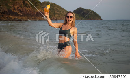 Woman stand knee-deep in sea on sunset. Girl on beach in green s Woman stand knee-deep in sea on sunset. Girl on beach in green s 86847501
