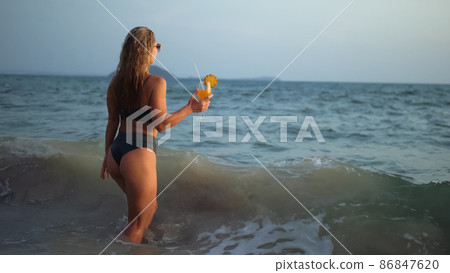 Woman stand knee-deep in sea on sunset. Girl on beach in green s Woman stand knee-deep in sea on sunset. Girl on beach in green s 86847620