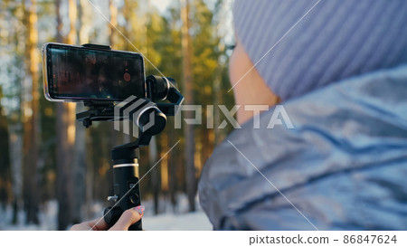 Professional Videographer Holding DSLR Camera on 3-axis Gimbal Stabilization Device in Winter. Cinematographer Operator. Slow Motion Professional Videographer Holding DSLR Camera on 3-axis Gimbal Stabilization Device in Winter. Cinematographer Operator. Slow Motion 86847624