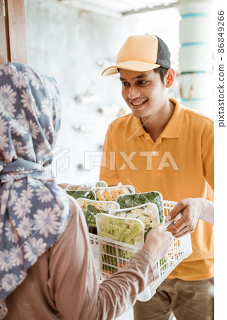 Deliveryman gives vegetable orders to women in headscarves 86849266