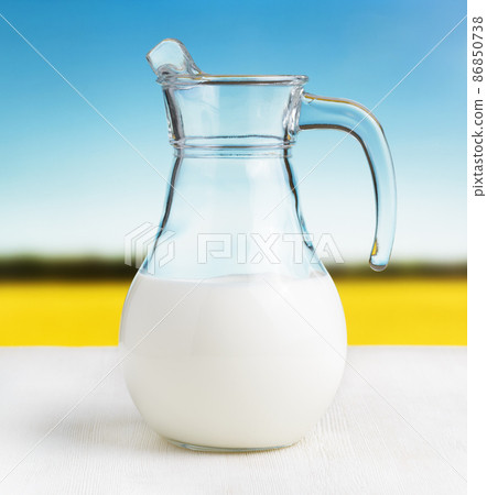 Jug of milk on meadow background. Half full pitcher Jug of milk on meadow background. Half full pitcher 86850738