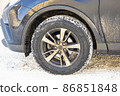 The wheel of a dirty car on a background of snow on a sunny winter morning. 86851848