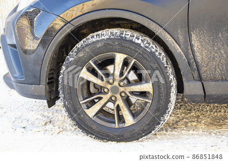 The wheel of a dirty car on a background of snow on a sunny winter morning. The wheel of a dirty car on a background of snow on a sunny winter morning. 86851848