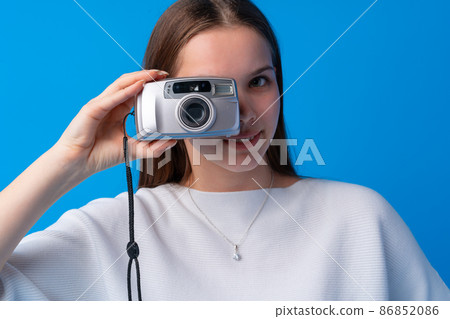 Young caucasian woman holding vintage camera on blue background in studio 86852086