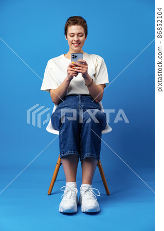 Cheerful attractive young woman holding smartphone, enjoying chatting or online shopping against blue background 86852104