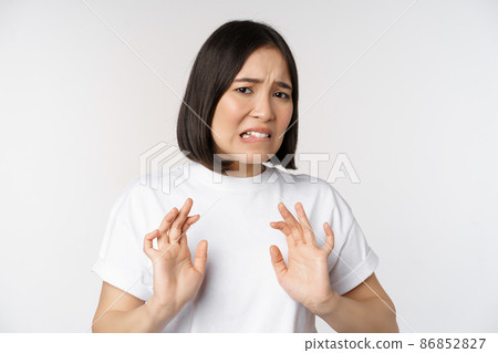 Disgusted asian woman rejecting smth, grimacing from dislike and aversion, stare with cringe, refusing offer, standing over white background 86852827