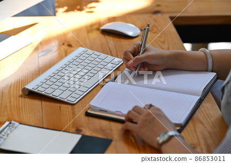 Cropped shot businesswoman working with computer and writing business plan on notebook. Cropped shot businesswoman working with computer and writing business plan on notebook. 86853011