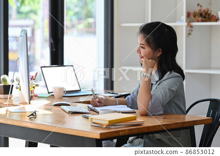Side view young asian woman sitting a her workplace and working with computer. Side view young asian woman sitting a her workplace and working with computer. 86853012