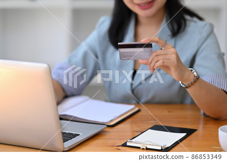 Satisfied young asian woman holding credit card and shopping online on computer laptop. 86853349
