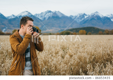 The man is a photographer in the field takes a picture on an old retro film camera. 86853435