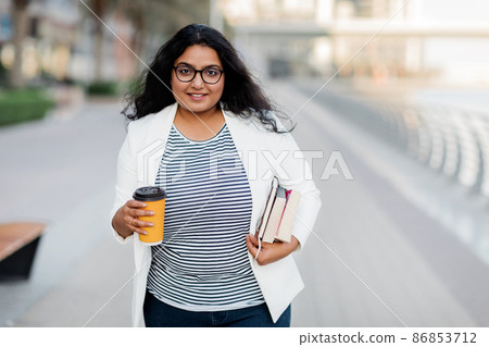 A beautiful young woman with a cup of coffee and books on the street. A beautiful young woman with a cup of coffee and books on the street. 86853712