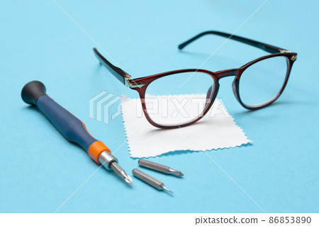 Glasses for vision, a lens cleaning cloth, and a screwdriver for repairs on a blue background. Glasses repair concept. Workshop. 86853890