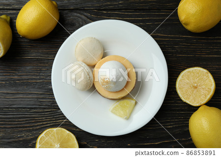 Plate with cupcake and macaroons, and lemons on wooden table 86853891