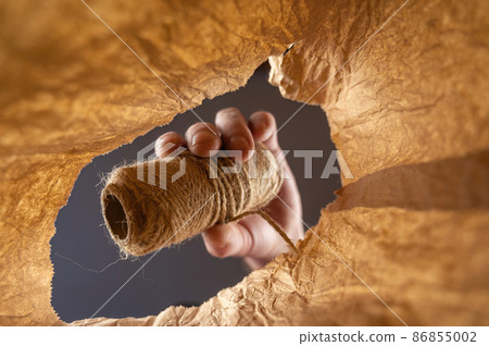 A hand places a skein of twine in a brown paper bag. A mature man's hand holds the jute thread. Shot from the bottom up. Close up. Selective focus. A hand places a skein of twine in a brown paper bag. A mature man's hand holds the jute thread. Shot from the bottom up. Close up. Selective focus. 86855002
