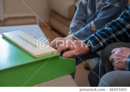 A grandfather teaches his grandson to play the toy piano. The elderly man's hands press the keys of a small children's musical instrument. 86855003