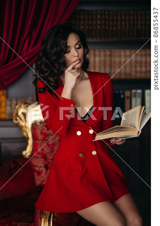 Elegant brunette in red sitting on and holding a Elegant brunette in red sitting on and holding a 86855437