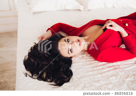 Sexy girl in red dress lying on bed with closed 86856818