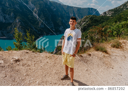 Guy traveler on the background The famous Piva Canyon with its fantastic reservoir. View of road above Piva Lake (Pivsko Jezero) in Montenegro. man looks at river Piva, Montenegro. 86857202