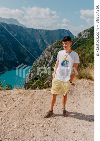 Guy traveler on the background The famous Piva Canyon with its fantastic reservoir. View of road above Piva Lake (Pivsko Jezero) in Montenegro. man looks at river Piva, Montenegro. 86857266