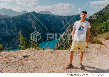 Guy traveler on the background The famous Piva Canyon with its fantastic reservoir. View of road above Piva Lake (Pivsko Jezero) in Montenegro. man looks at river Piva, Montenegro. 86857282