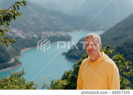 Man - Traveler on the background The famous Piva Canyon with its fantastic reservoir. View of road above Piva Lake (Pivsko Jezero) in Montenegro. man looks at river Piva, Montenegro. 86857350