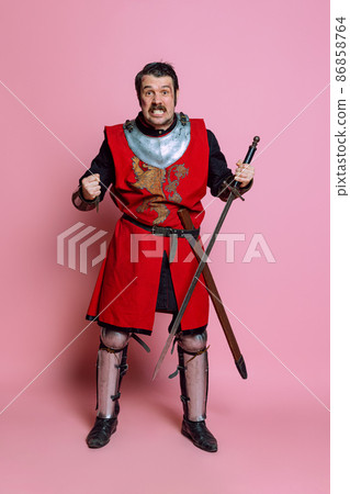 One young man, medieval warrior or knight wearing wearing armor clothing posing isolated over pink background. Comparison of eras, history, emotions 86858764