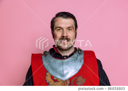 One young happy man, medieval warrior or knight wearing wearing armor clothing posing isolated over pink background. Comparison of eras, history, emotions One young happy man, medieval warrior or knight wearing wearing armor clothing posing isolated over pink background. Comparison of eras, history, emotions 86858803