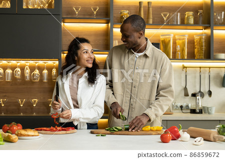 Young couple talks cutting fresh vegetables for salad Young couple talks cutting fresh vegetables for salad 86859672