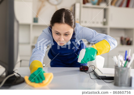 Girl cleans up the desktop in the office with a rag and cleaning products Girl cleans up the desktop in the office with a rag and cleaning products 86860756