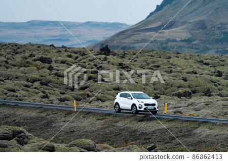 White car driving through vast lava fields covered by moss 86862413